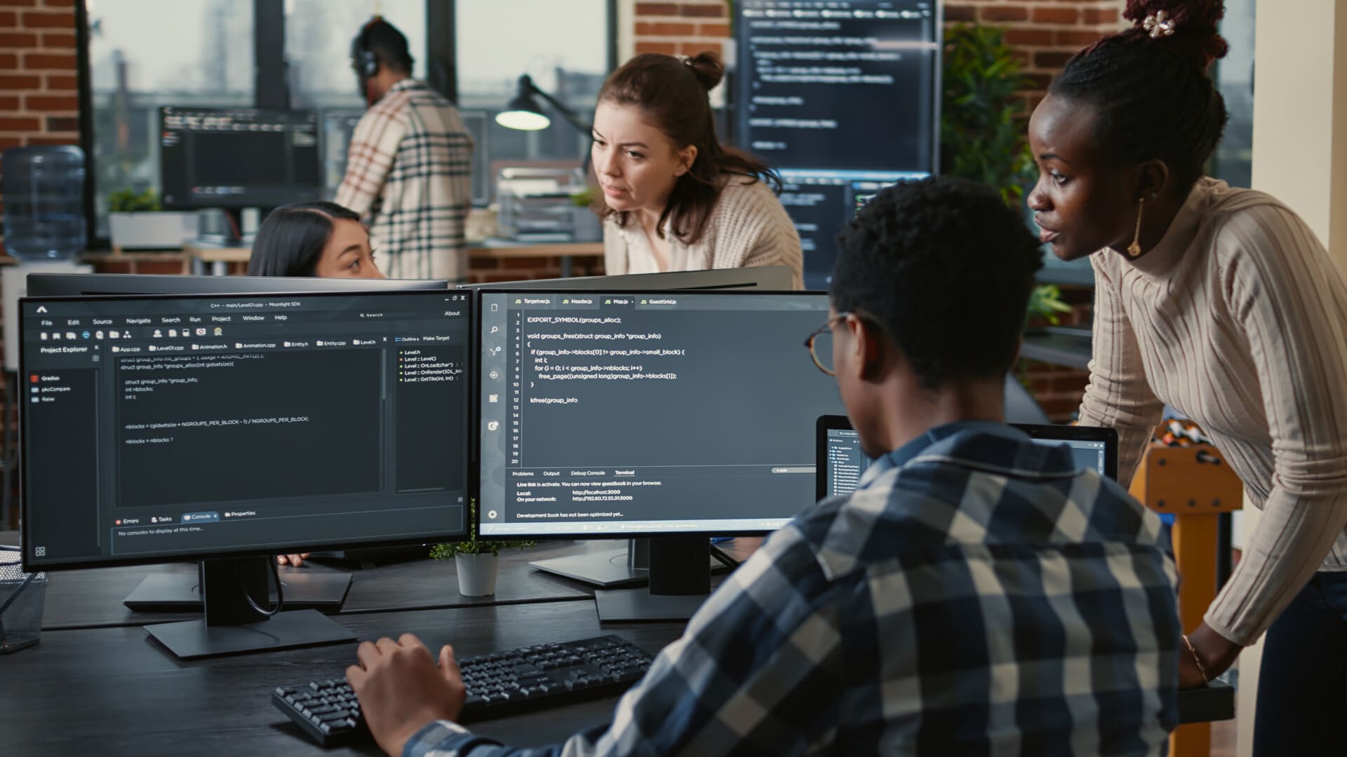 Mixed team of artificial intelligence cloud programers talking about programming in front of multiple screens